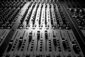 Black & white closeup of a mixing console's faders, illustrating our high-quality radio ad services.