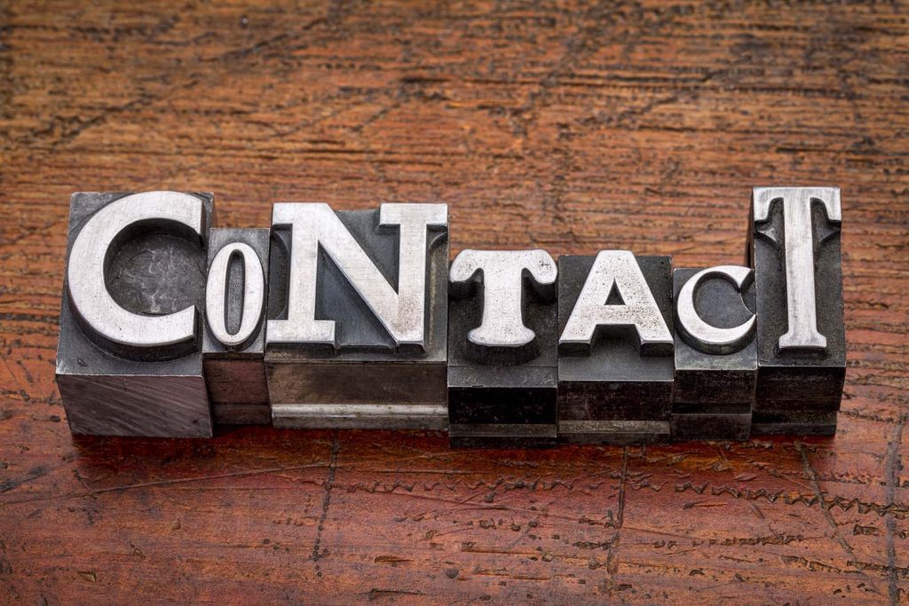 Stamp pad blocks spelling "Contact" on a wooden table with purple tint.